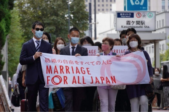 画像。結婚の自由をすべての人に訴訟、東京第一次訴訟入廷行動の様子。原告たちを先頭にして、笑顔を見せながら東京地方裁判所前の沿道を歩いている。