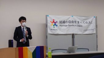 綱森史泰弁護士が、マイクを持ちながら、2022年11月30日に下されたと今日判決に
ついて話をしている。「結婚の自由をすべての人に Marriage Equality in Japan
北海道訴訟原告弁護団」と書かれた旗が掲げられている。