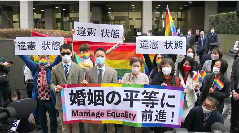 第一審判決直後、東京地裁前で「違憲状態」「婚姻の平等に前進」と書かれた旗を掲げる「結婚の自由をすべての人に」東京１次訴訟の原告・弁護団と支援者たち