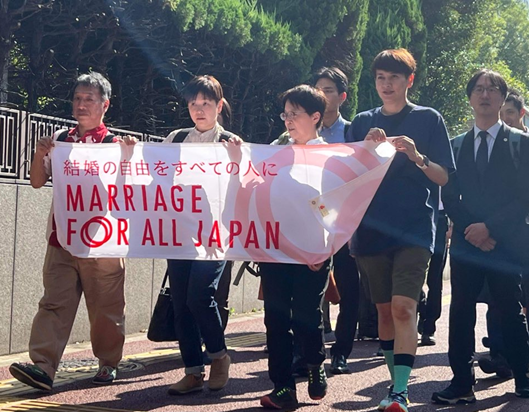 Marriage For All Japanのフラッグを掲げて東京地方裁判所入口に向かう「結婚の自由をすべての人に」東京２次訴訟原告と代理人弁護士たち