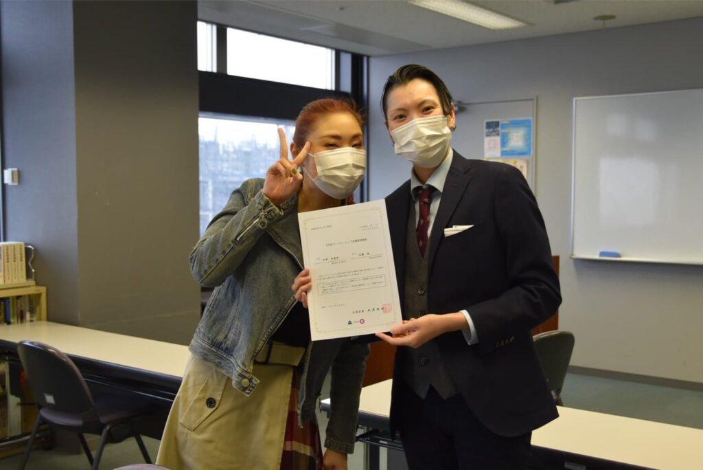 文京区でパートナーシップ制度を利用した近藤さんと今井さん　ピースさんを出して喜びの表情