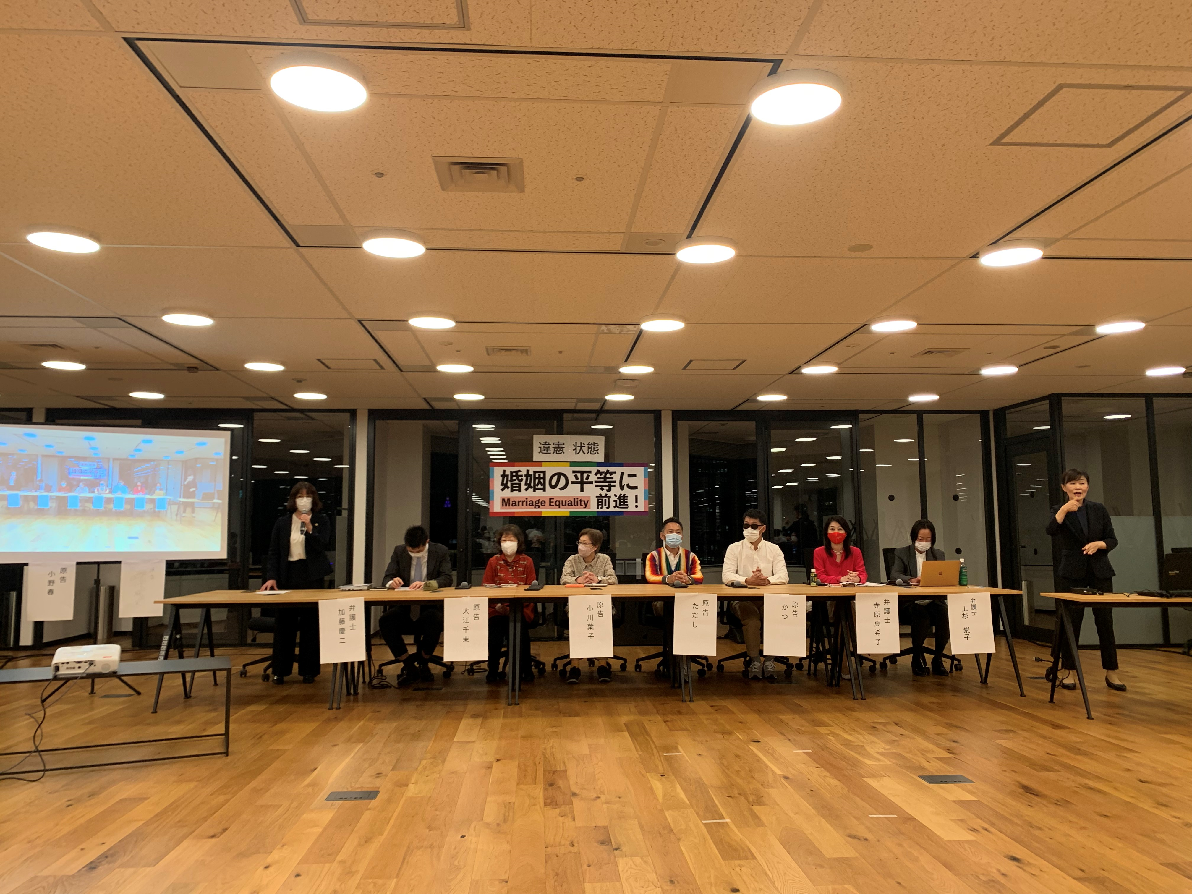 ④ 記者会見・判決報告会に椅子に座って臨む東京一次訴訟原告４名（大江さん、小川さん、ただしさん、かつさん）と弁護団員、手話通訳者の様子