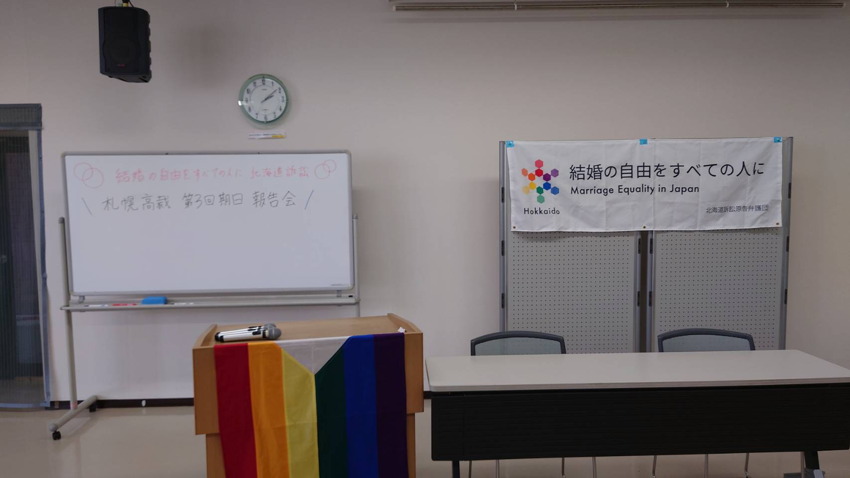 ホワイトボードに「結婚の自由をすべての人に北海道訴訟 札幌高裁 第３回期日 報告会」と書かれている。「結婚の自由をすべての人に Marriage Equality in Japan 北海道訴訟原告弁護団」と書かれた旗が掲げられている。