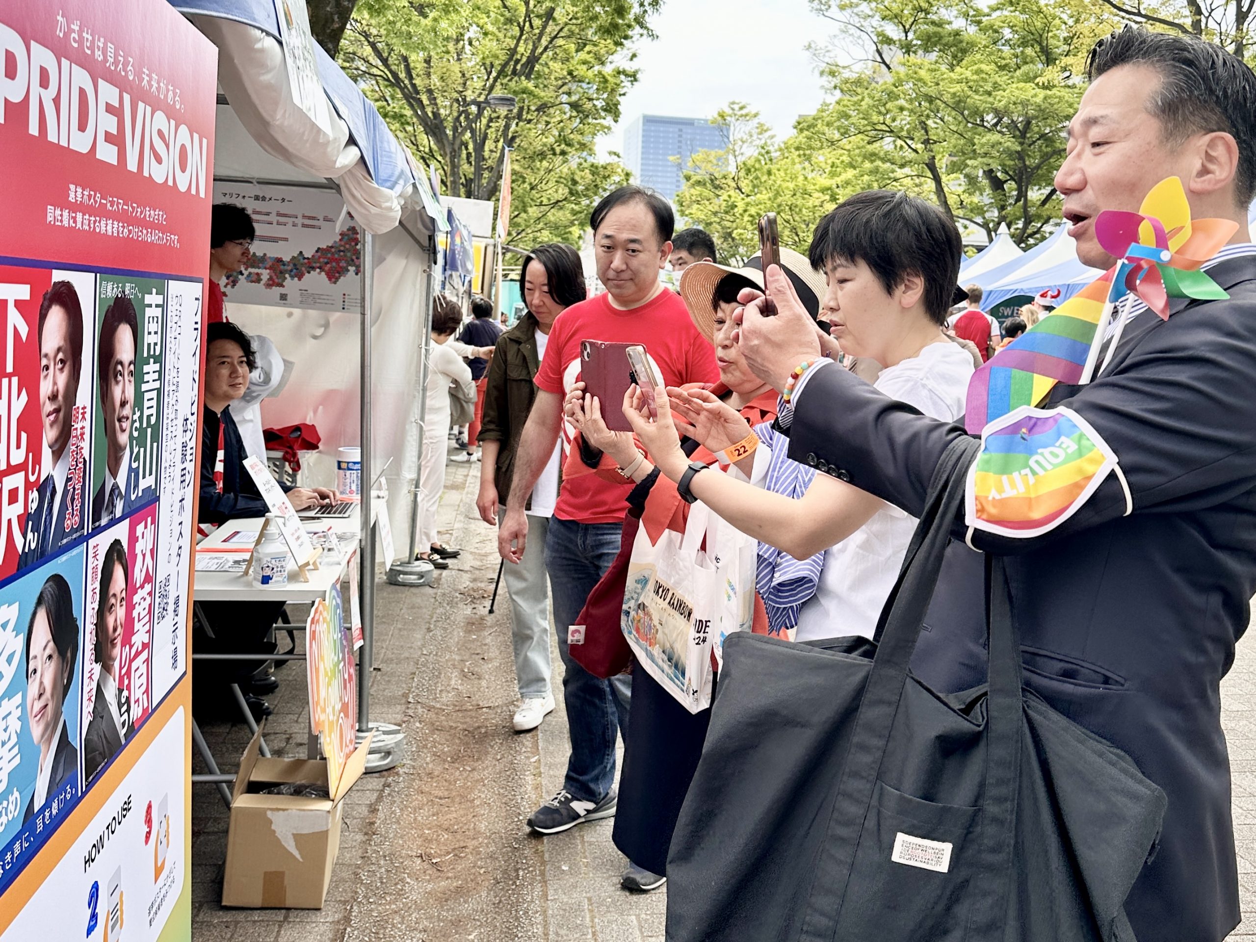 東京レインボープライド2024のマリフォーブース前にて、選挙ポスターにスマートフォンをかざすと、結婚の平等（同性婚）法制化に賛成の候補者を見分けられるARカメラ「PRIDE VISION（プライドビジョン）」を体験する、立憲民主党の福山哲郎参議院議員・尾辻かな子さん・社民党の福島みずほ参議院議員