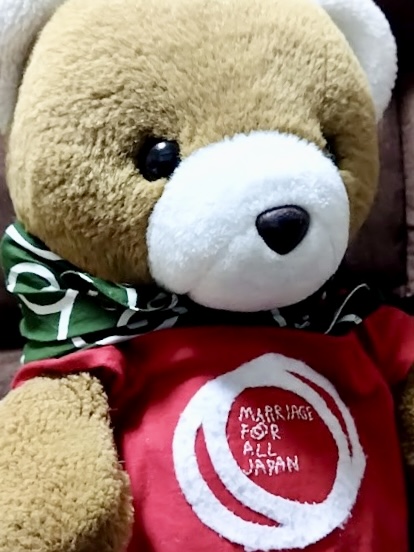 クマのぬいぐるみがTシャツを着ている。 シャツには、MARRIAGE FOR ALL JAPANの文字とロゴが刺繍されている。