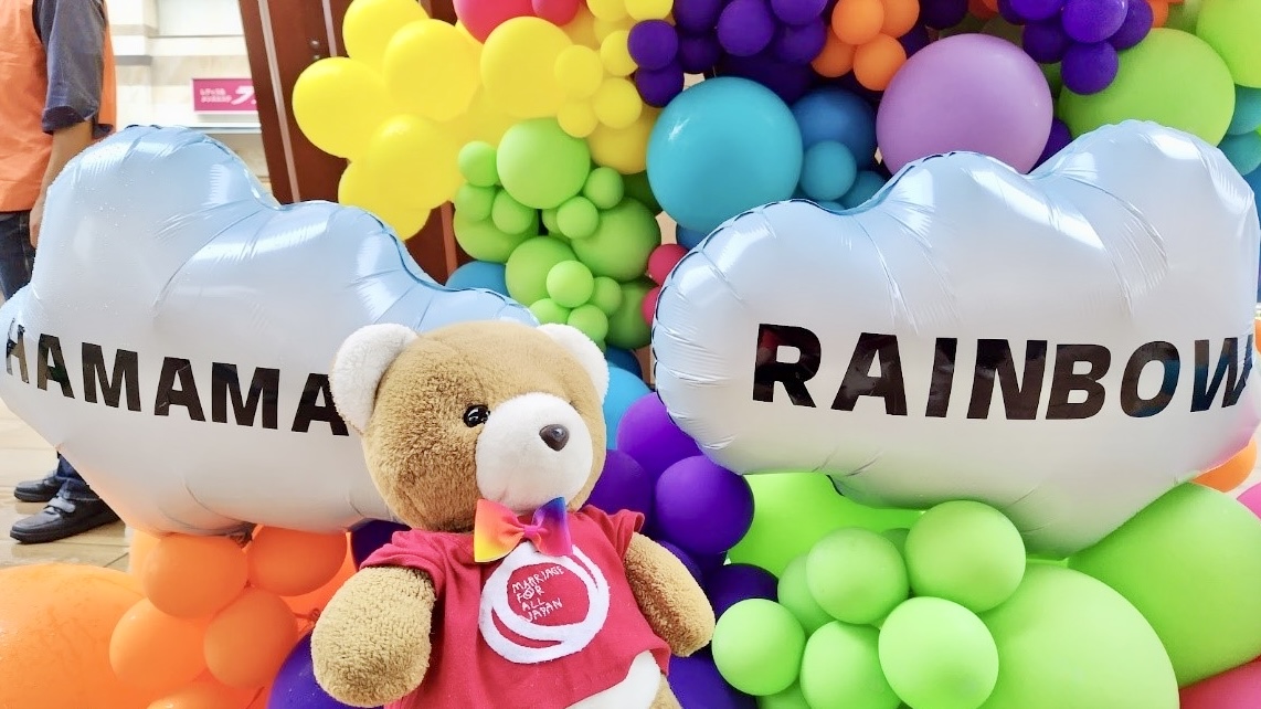 様々な色・大きさのバルーンが無数に飾られている。 雲の形のバルーンには「HAMAMATSU RAINBOW」と印字されている。 バルーンの手前でくまがうっとりしている。 くまは、マリフォーのロゴが入ったシャツを着ている。