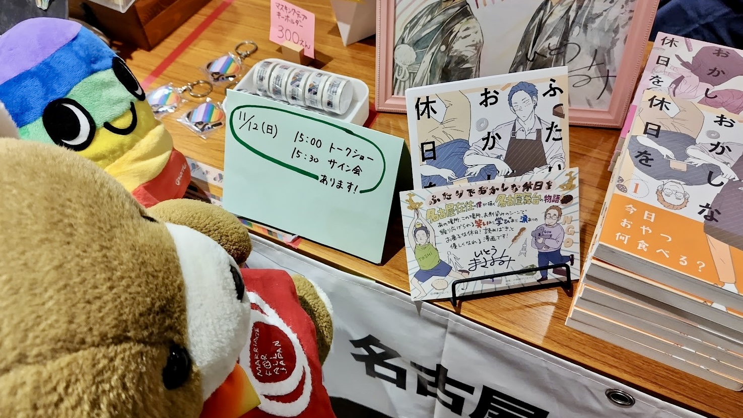 ゲイカップルを描いた漫画「ふたりでおかしな休日を」が飾られている。 漫画家さんのトークショーとサイン会があることを知らせる手書きの案内文も置かれている。 案内文の前で、くまがぶらんちゃんに漫画の紹介をしている。