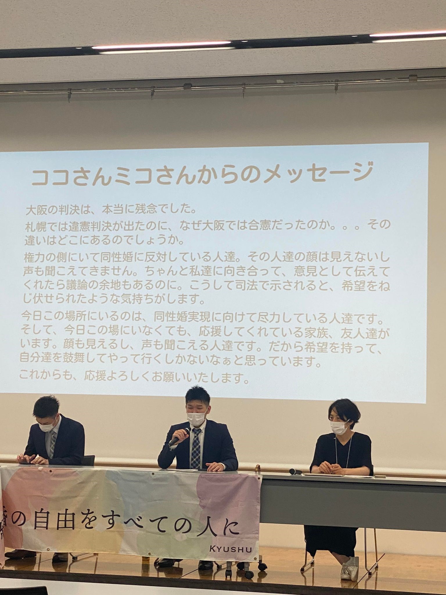 報告会の様子 ココさんとミコさんのメッセージが背景に映っており、その前に、3人の人が座っている。マイクを持ってこうすけさんが話している。 ココさんとミコさんのメッセージは以下のとおり。大阪の判決は、本当に残念でした。 札幌では違憲判決が出たのに、なぜ大阪では合憲だったのか。。。その違いはどこにあるのでしょうか。 権力の側にいて同性婚に反対している人達。その人達の顔は見えないし声も聞こえてきません。ちゃんと私達に向き合って、意見として伝えてくれたら議論の余地もあるのに。こうして司法で示されると、希望をねじ伏せられたような気持ちがします。 今日この場所にいるのは、同性婚実現に向けて尽力している人達です。そして、今日この場にいなくても、応援してくれている家族、友人達がいます。顔も見えるし、声も聞こえる人達です。だから希望を持って、自分達を鼓舞してやって行くしかないなぁと思っています。 これからも、応援よろしくお願いいたします。