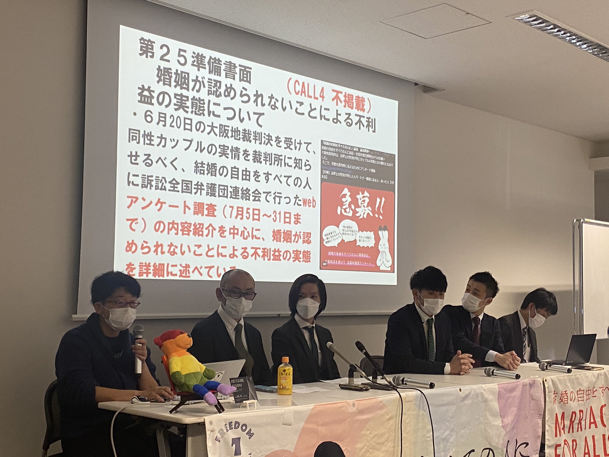 記者会見の様子。原告さん4人と弁護団2人が並んでいる。後ろには裁判に提出された書類の紹介がされている。
