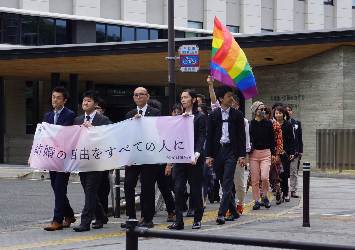 結婚の自由をすべての人にと書かれた九州訴訟の横断幕を持って裁判所へ歩く原告と弁護団。レインボーフラッグもはためいている。