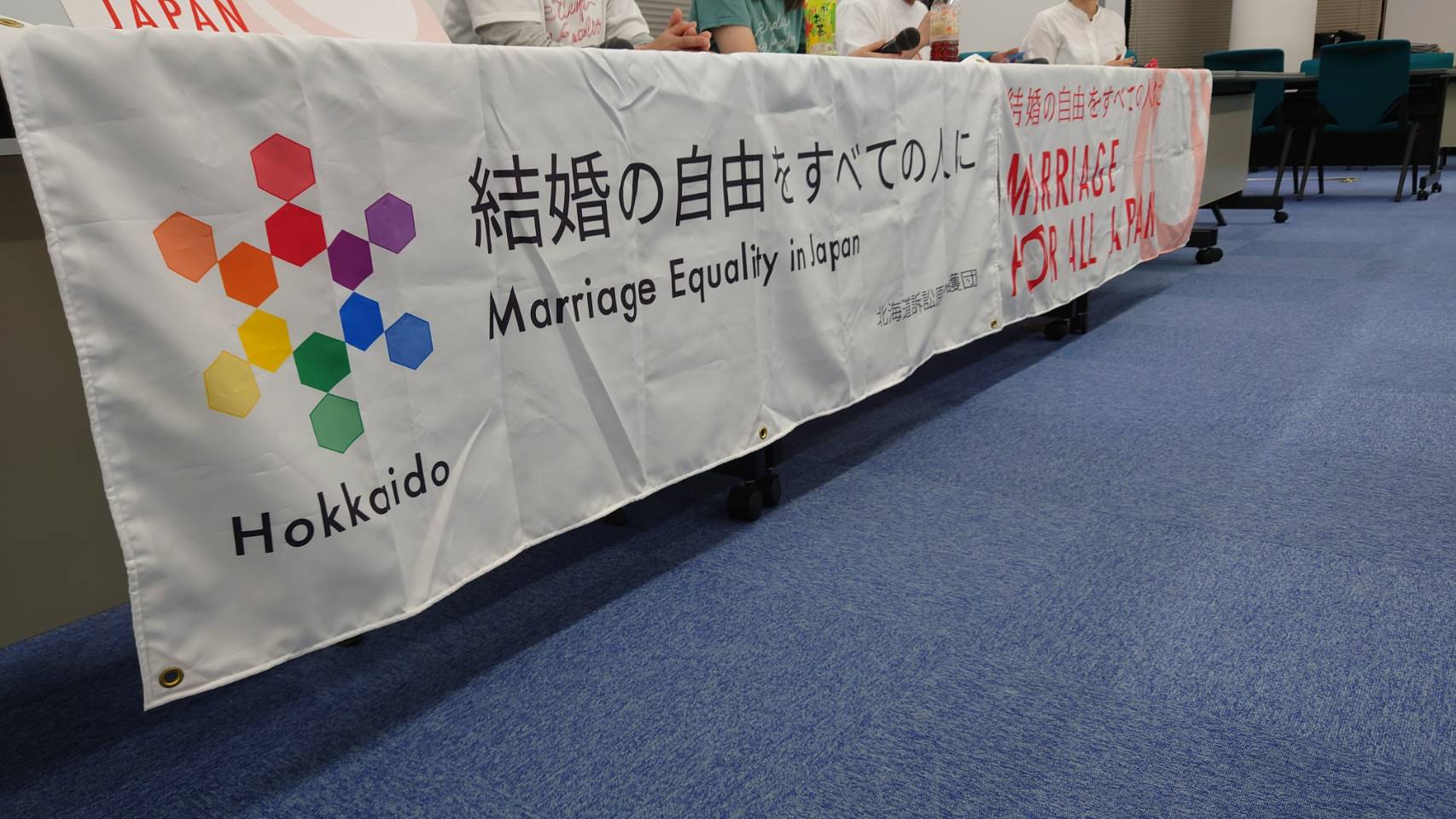 札幌地方裁判所の前で、「結婚の自由をすべての人に」北海道訴訟の原告と弁護団、支援者が、「高裁でも違憲！早く立法すればいいしょ」と書かれた横断幕やレインボーカラーの旗を掲げている