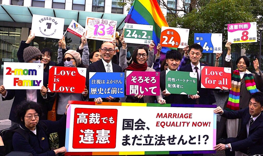 12月13日、福岡高裁前。同性婚ができないことは憲法13条、14条1項、24条2項に違反するとの判決がなされました！ そのことを、裁判所前から伝えてる写真です。笑顔がたくさん見えます。 九州訴訟の原告、弁護団が横断幕やボードを持っています。 大きなメッセージは、 高裁でも違憲 国会、まだ立法せんと！？ 原告さんのメッセージは左から、 ・2-mom Family (母2人家族) ・Love is Love 原告ココさんとミコさんから。 ・注視はよかけん 歴史ば前に こうぞうさん ・そろそろ聞いて ゆうたさん ・同性パートナーも配偶者に こうすけさん ・Love For All まさひろさん 後ろの弁護団のボード 左から ・九州訴訟のロゴマーク(FREEDOM of marriage for all アルファベットの間には九州がデザインされています。) ・全国初13条 (間に見えてるのは、マリフォーの結婚の平等にYESの旗です。) ・憲法24条2項違反 ・憲法24条違反 ・憲法14条違反 ・違憲判断全国8件目