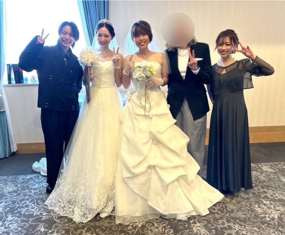 結婚式のドレスを着た女性二人と、友人３人が 並んでいる。 笑顔でポーズをとっている。