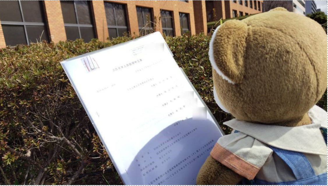 名古屋高裁の建物前で、くまちゃんが「上告状兼上告理由書」というタイトルの書類を持っている写真
