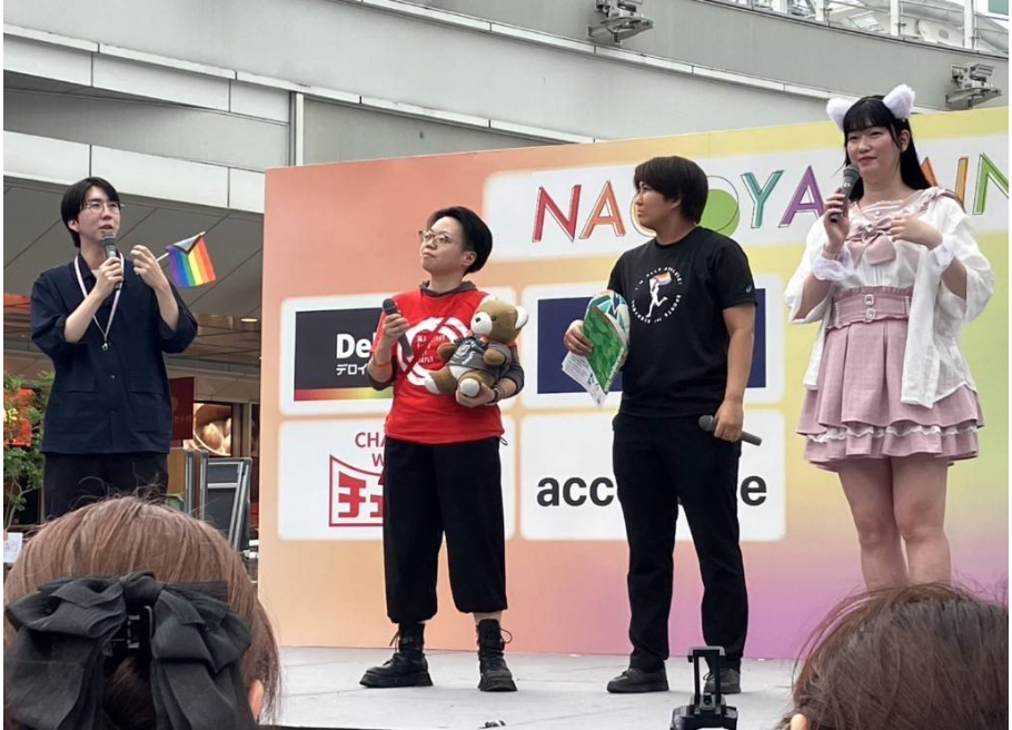 名古屋レインボープライドのステージに４人の人が並んでいる。 中央の人物がくまちゃんを抱いてる。