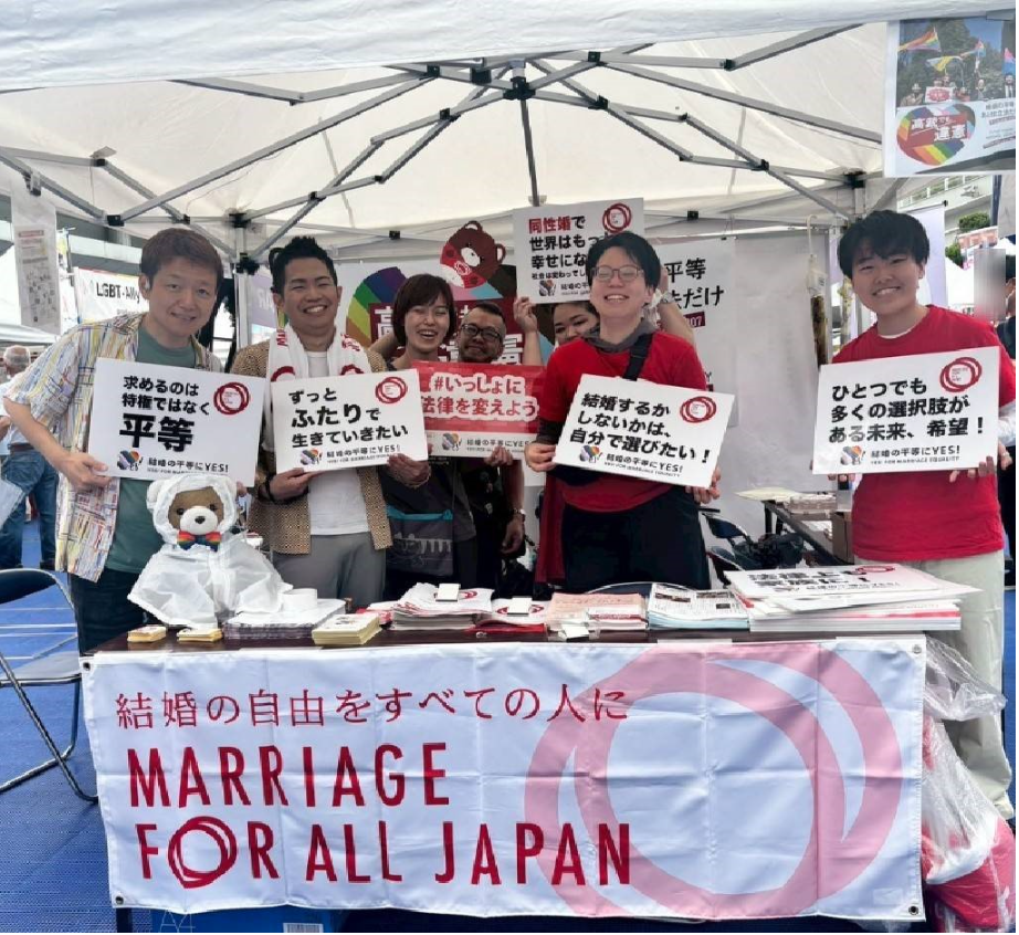 マリフォーブースの写真。「結婚の自由をすべての人に」と書かれた幕がかかっていて、７人のブーススタッフとくまちゃんが笑っている集合写真。