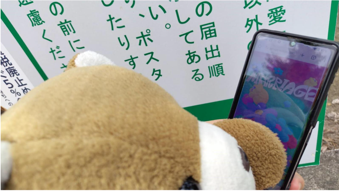 掲示板の前でスマホを操作するくまちゃん