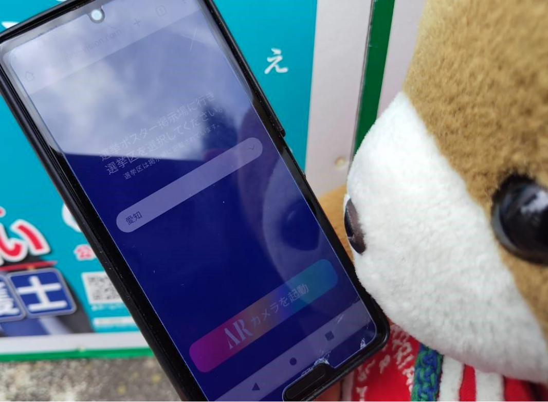 くまちゃんのスマホに、「選挙区を選択してください」という案内と、ARカメラを起動するというアイコンが表示されている。
