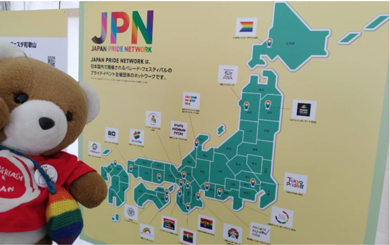 ジャパンプライドネットワークが作成したパネルを眺めるくまちゃん。日本地図に、各地のプライドイベントが書きこまれていて、各地でイベントが開催されているのがわかる。