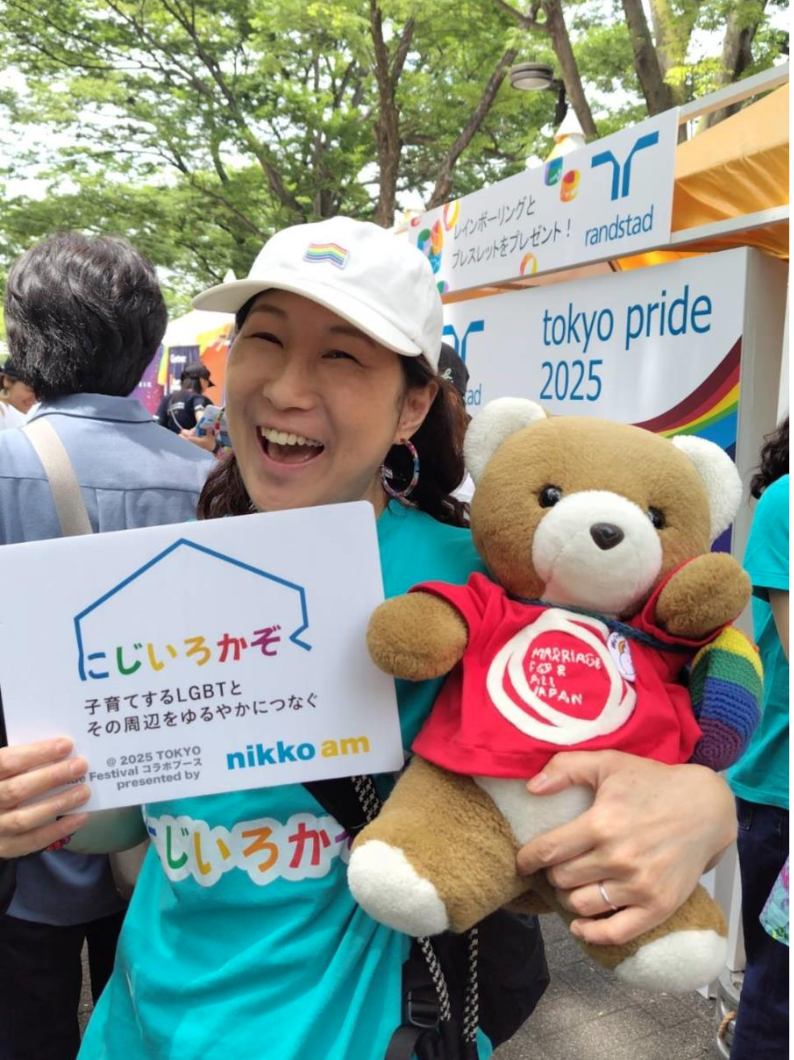 くまちゃんと原告おのはるさんの写真。 おのはるさんは、にじいろかぞくと書かれたボードを持っている。