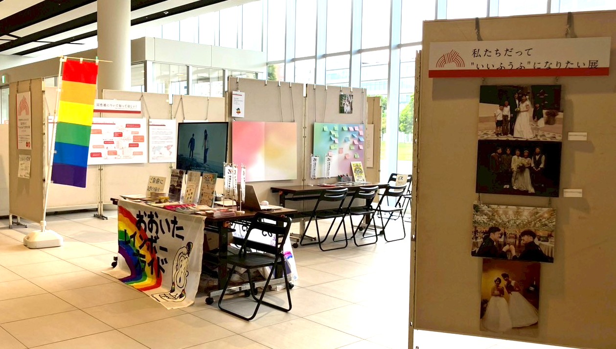 パネル展の様子。子どもを育ててきた同性カップルのパネルなど写真が飾られている。また、受付の机には主催団体のおおいたレインボープライドの横断幕が飾られ、チラシなども置かれている。