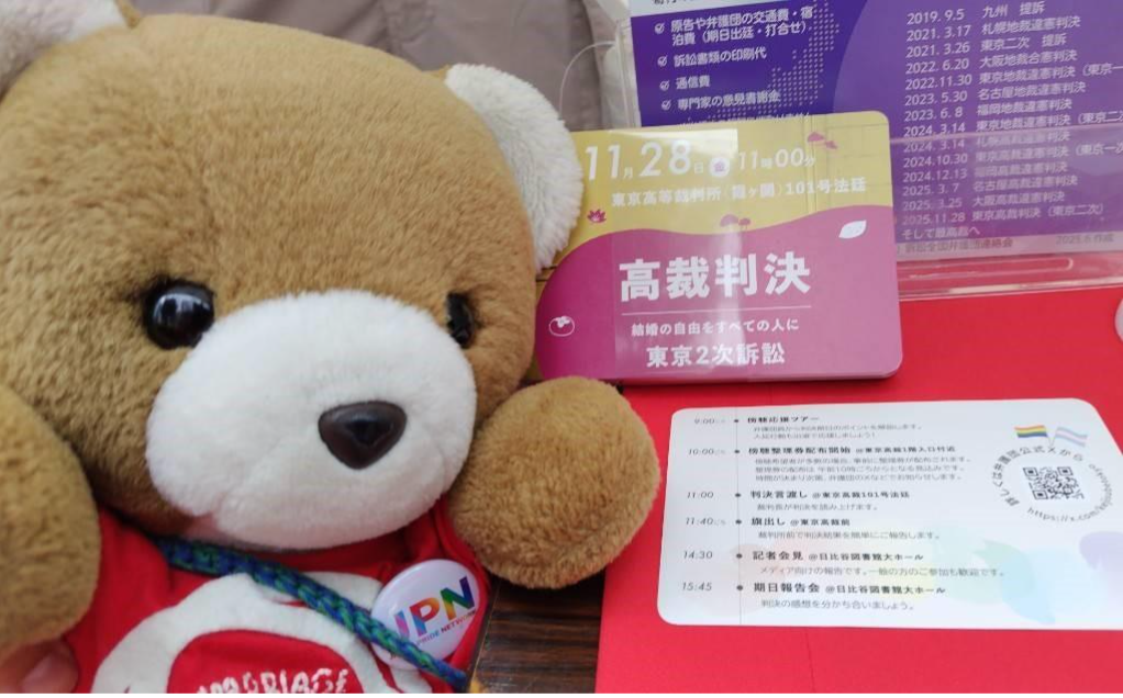 マリフォーブースのテーブルに、東京２次訴訟の東京高裁判決を告知するポストカードが置かれている。くまちゃんがカードを並べてうれしそうにしている。