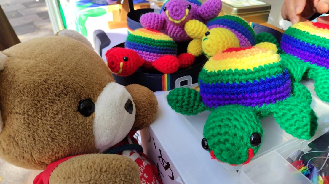 カメのぬいぐるみたちとくまちゃんがあいさつしている写真。 カメの甲羅はレインボーカラーになっている