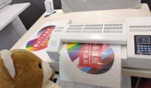 プラカードを防水加工するための機械に入れて、機械を操作するくまちゃん。