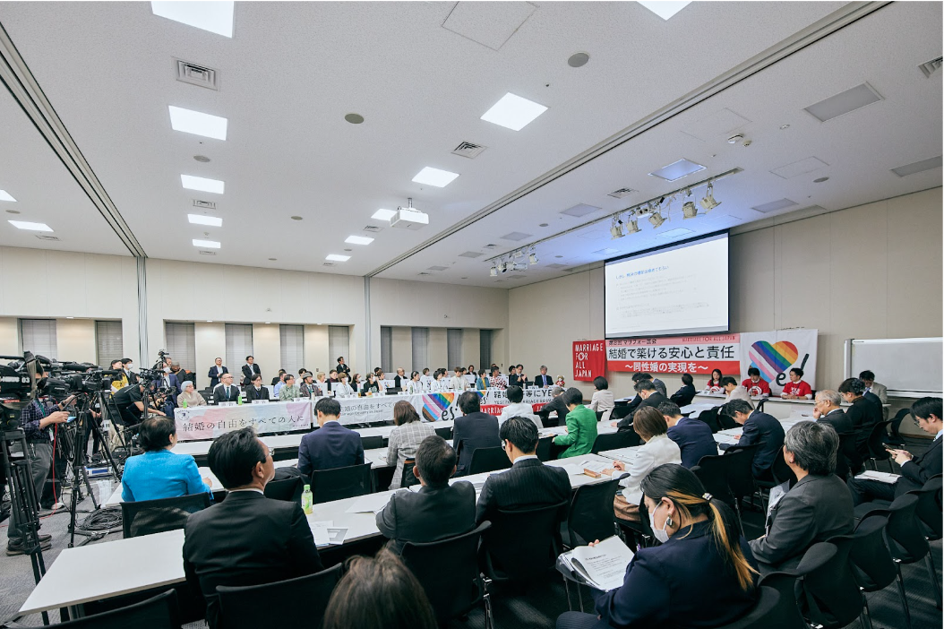 会議室で行われている「第8回 マリフォー国会」の会場全体の様子。左側にはテレビ局などの報道カメラが多数並び、多くの参加者が席を埋めている。前方には「結婚で築ける安心と責任 〜同性婚の実現を〜」という横断幕が掲げられ、壇上のパネリストたちが議論を行っている。