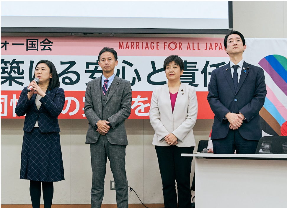 「第8回 マリフォー国会」のステージに並んで立つ4名の登壇者。背景には「結婚で築ける安心と責任」というイベントタイトルが掲げられている。マイクを持って挨拶をする女性や、それを見守るスーツ姿の国会議員たちの立ち姿。