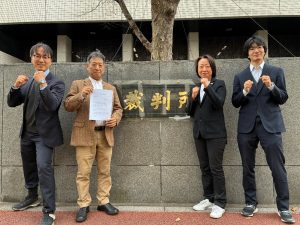 東京高等裁判所の前で、上告状をもって立っている原告山縣さんと弁護団３名の写真
