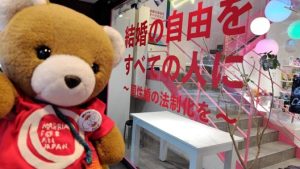 マリフォーくまちゃんが、ラッシュの店舗の前にいる。店舗の大きな窓に、結婚の自由をすべての人に、同性婚の法制化を、と書かれている。